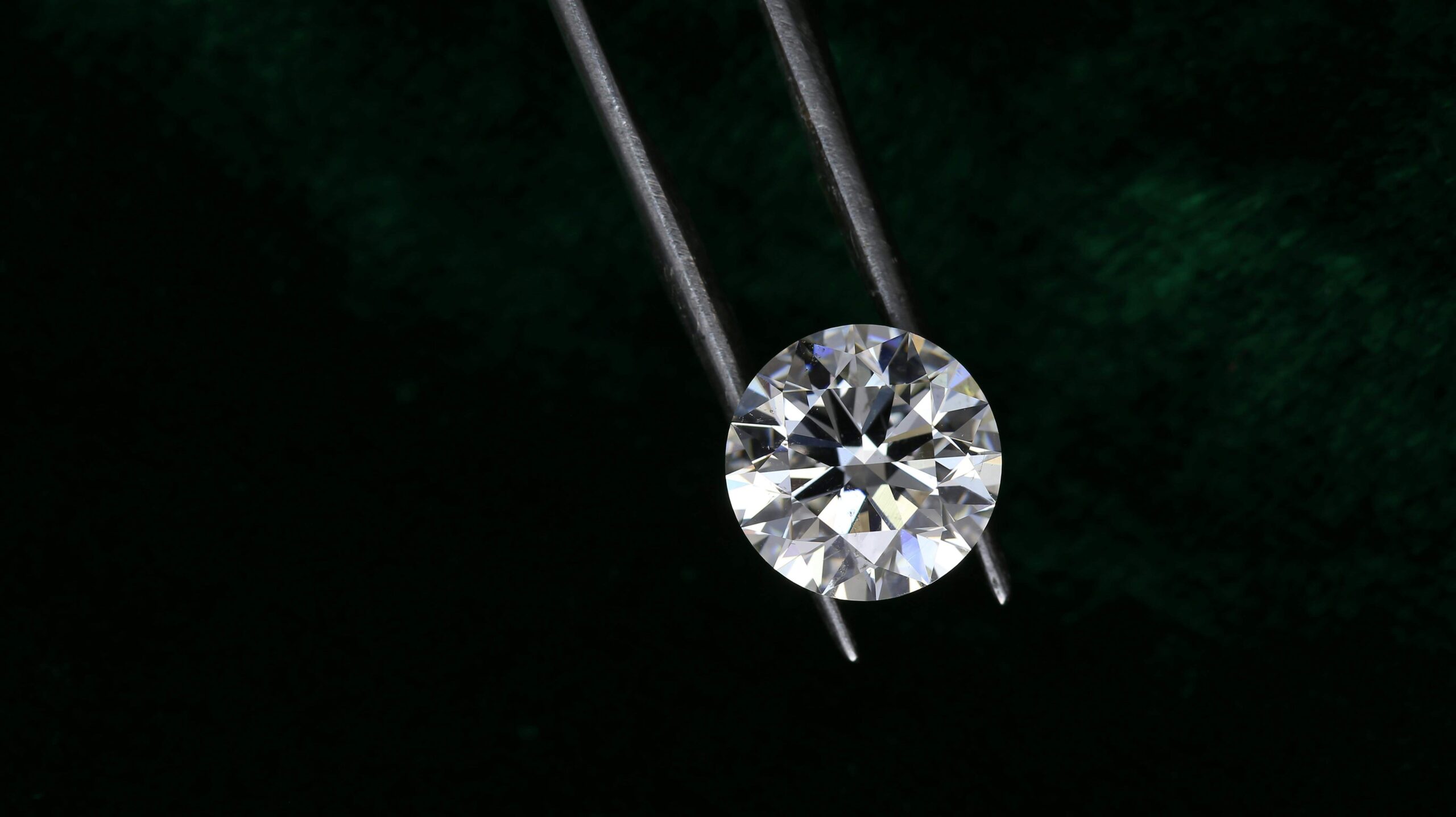 Round diamond stone held by a tweezer on a dark background